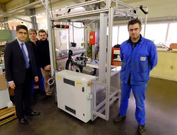 Quatre hommes posent autour d’une machine industrielle dans un atelier.