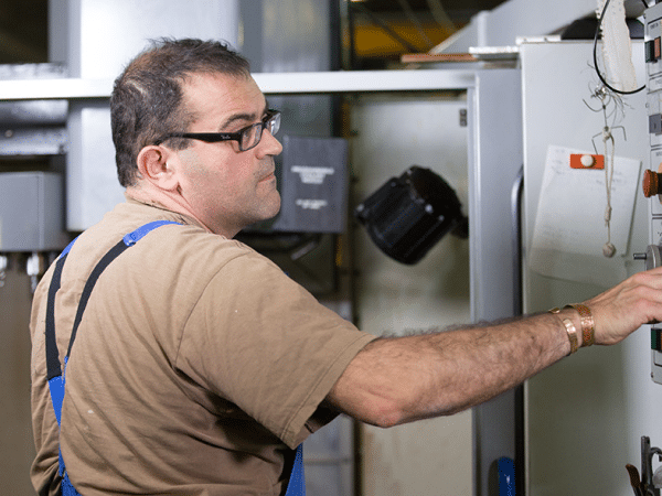 Technicien d'ACM supervisant le fonctionnement d'une machine industrielle, vêtu d'une salopette bleue.