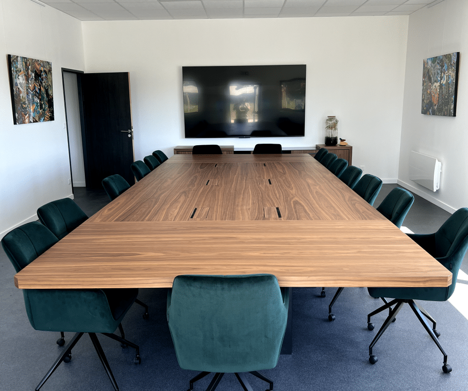 Salle de réunion moderne avec une grande table en bois, des chaises vertes, et un écran plat au mur, située chez ACM.