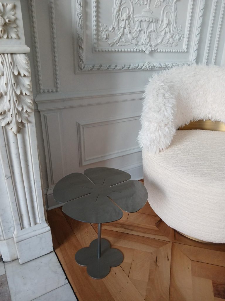 Une table basse design en forme de trèfle à quatre feuilles placée près d’un fauteuil et d’une cheminée décorée.